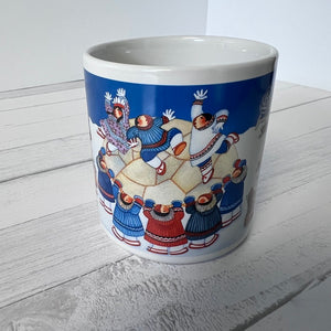 Ceramic mug with a colorful design of people on a blue background, placed on a wooden surface.