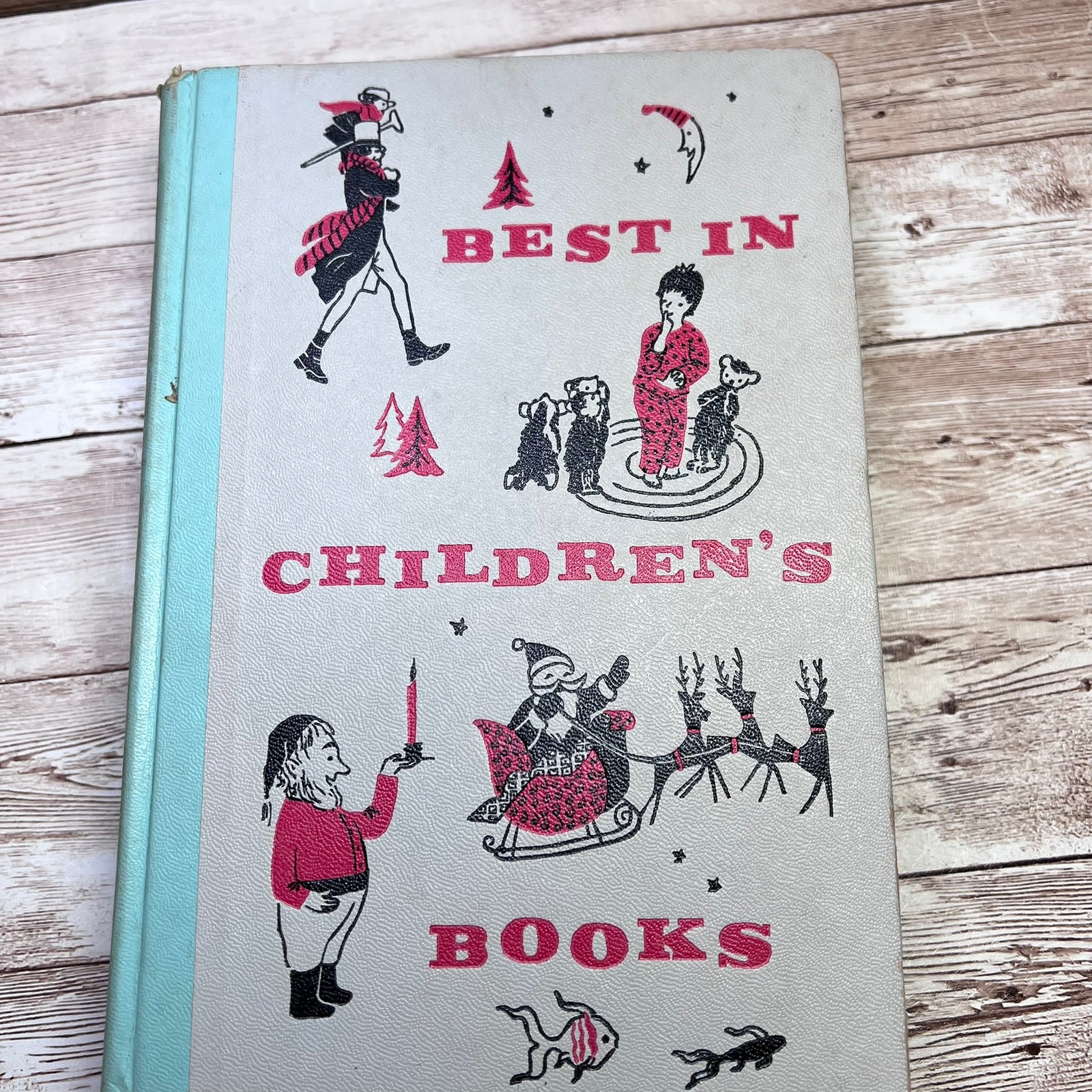 Vintage hardcover children's book titled 'Best in Children's Books' with illustrated holiday scenes on a light cover and a pale blue spine, photographed on a rustic wood surface.