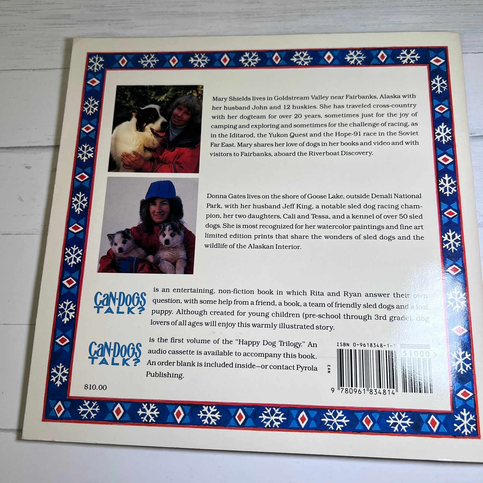 Back cover of the children's book 'Candy Cogs' by Pynxa Publishing, featuring a colorful snowflake-patterned border and a central illustration of a dog on a snowy hill.