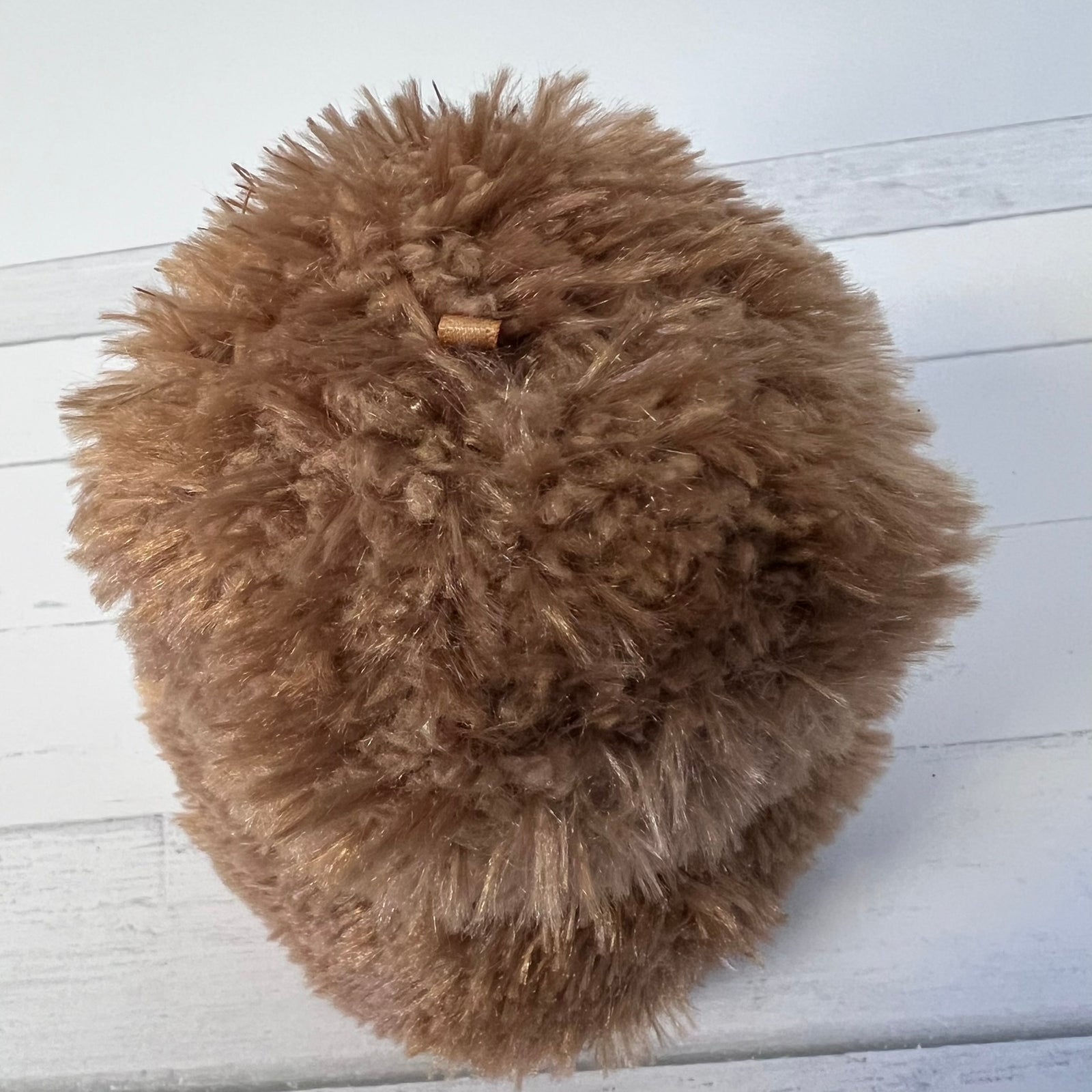 Brown fluffy pom-pom on a white wooden surface