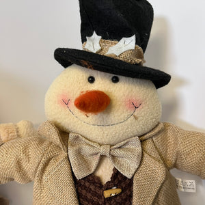 Stuffed snowman toy with a top hat, bow tie, and coat on a white background