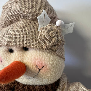 Stuffed animal wearing a burlap hat with a flower and leaves on a blurred background