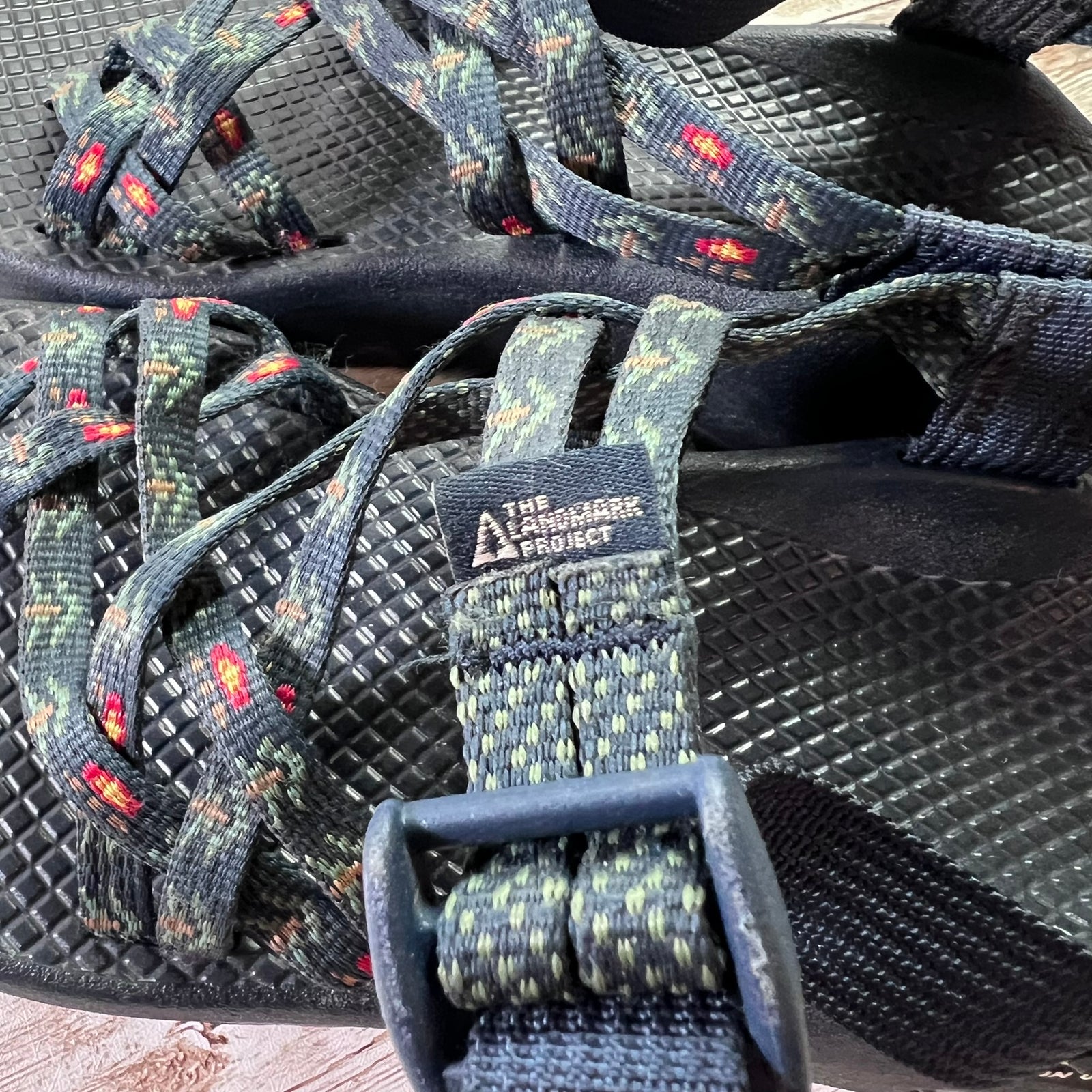 Close-up of a pair of Larchmont & Project athletic sandals with dark textured soles and patterned straps in green, gray, and red.