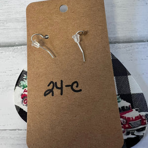 Clear earrings on a brown cardboard card with '24-C' writing, against a checkered fabric background.