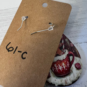 Pair of silver earrings on a brown card with a decorative item in the background