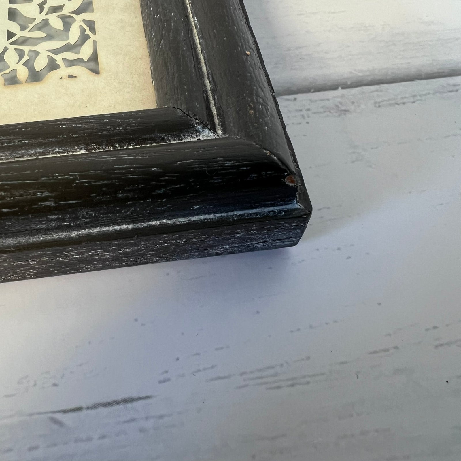 Close-up of a black distressed wooden picture frame corner on a white painted wood surface.