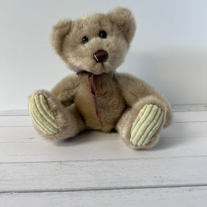 Beige teddy bear with a brown ribbon on a white wooden surface