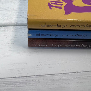 Three 'darby conley' boxes stacked on a light wooden surface