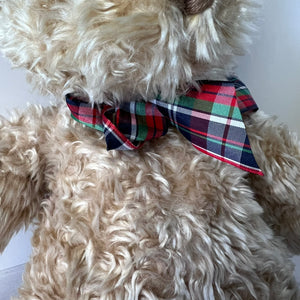 Beige teddy bear wearing a plaid bow tie on a white background