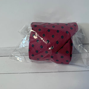 Red tie with black polka dots in clear plastic packaging on a white wooden surface
