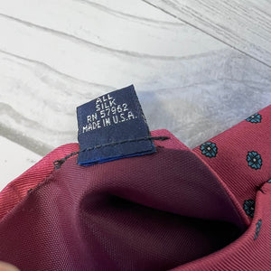 Fabric tag on a red fabric with floral patterns, indicating 'All Silk' and 'Made in U.S.A.'