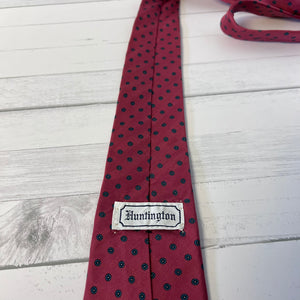 Red tie with black polka dots and 'Huntington' label on a light wooden surface