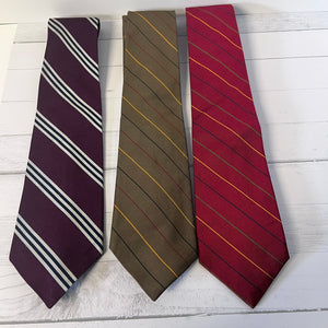 Three striped ties in purple, brown, and red on a light wooden surface