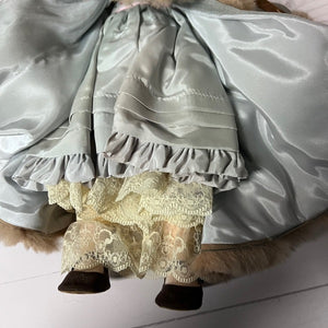 Close-up of a doll with a gray ruffled dress and lace hem on a white background