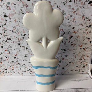 Ceramic vase shaped like a flower with a striped base against a textured wall.