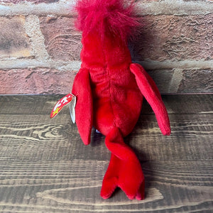 Red plush toy with a TY tag on a wooden surface and stone wall background