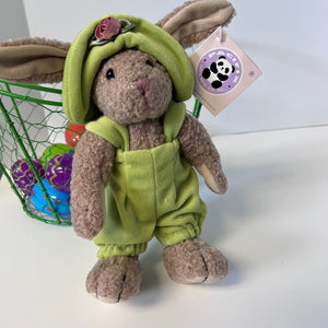 Stuffed toy rabbit in a green outfit with a tag, standing next to a basket of Easter eggs.