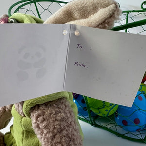 Open card with 'To' and 'From' fields held by plush toys in a green basket.