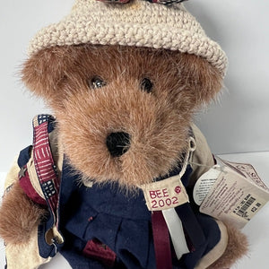 Teddy bear wearing a knitted hat and outfit with visible brand tag on a white background
