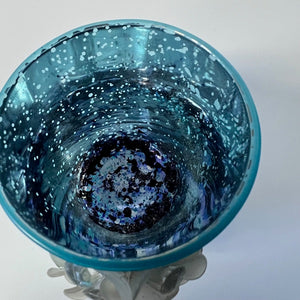 Blue glass candle holder with a white speckled pattern on a white background