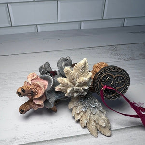 Decorative elements including a small bear, leaf-like structures, and a metallic object on a light wooden surface.