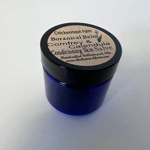 Blue jar with black lid labeled 'Chickenmash Farm Botanical Balm' on a white background