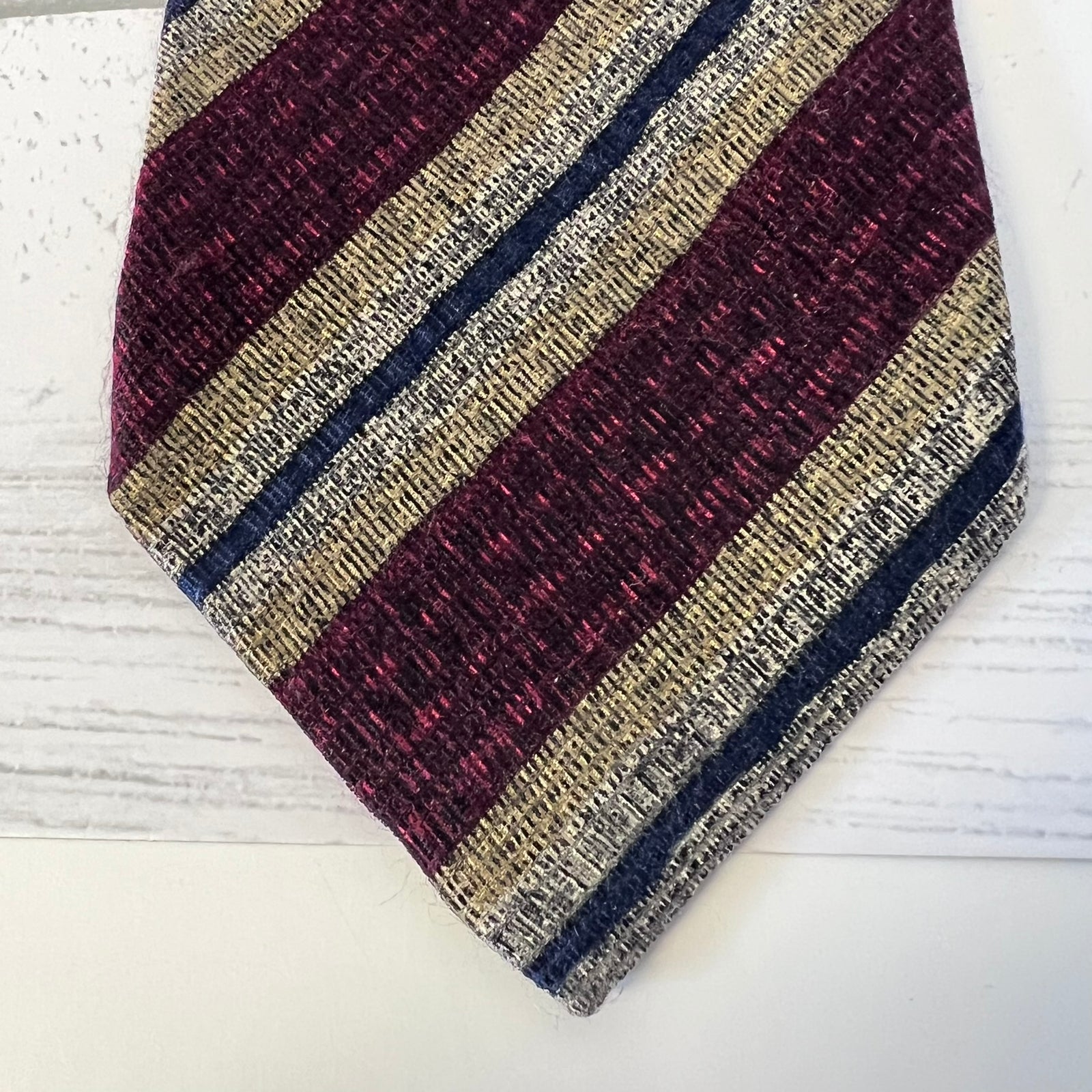 Striped tie with maroon, beige, and navy pattern on a white surface