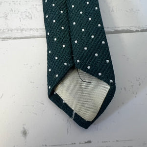 Dark green tie with white polka dots on a light gray surface