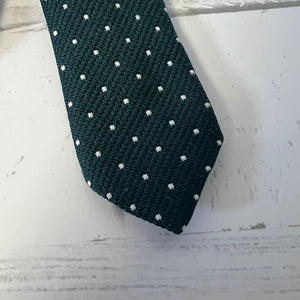 Dark green tie with white polka dots on a light wooden surface