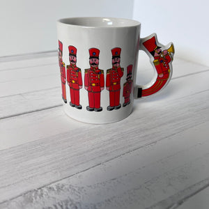 White mug with red soldier design on handle and sides, placed on a light wooden surface.