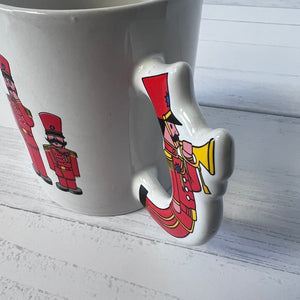 White mug with a decorative handle shaped like a nutcracker on a white wooden surface.