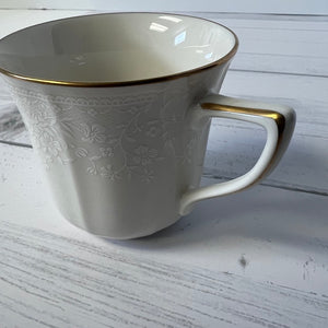 White mug with gold rim and handle on a light wooden surface