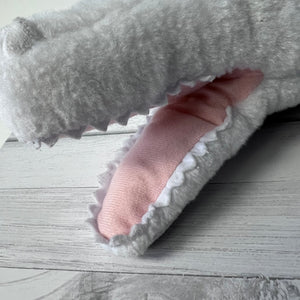 Gray plush toy with a pink interior on a wooden surface