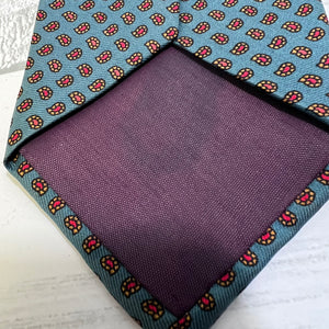 Purple pocket square with a blue patterned border on a white surface