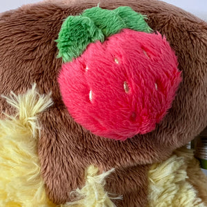 Plush toy resembling a brown bear with a red strawberry on its head