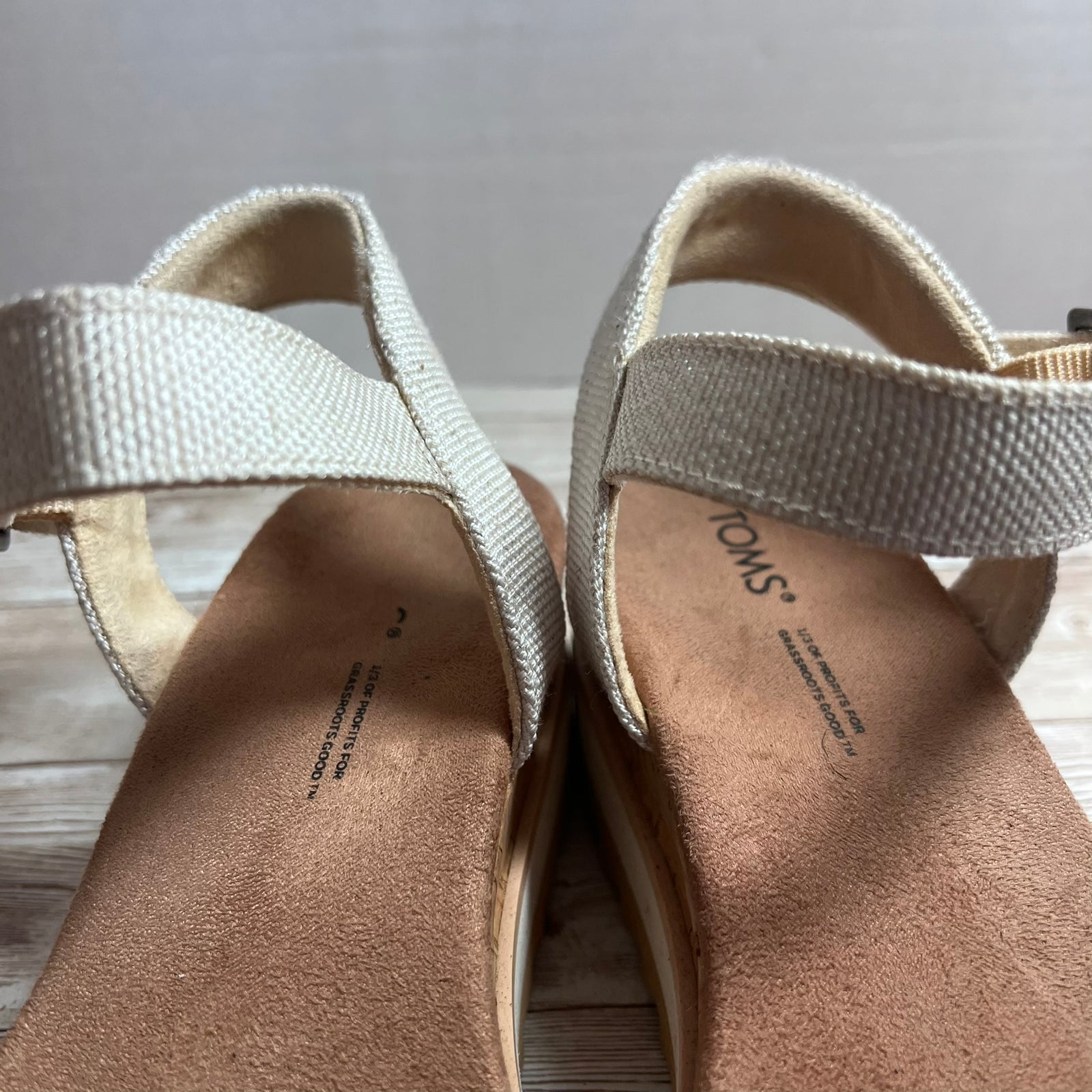 A pair of TOMS woven elastic sandal straps with a tan suede footbed and wedge, shown from a close-up angle.