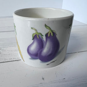 White pot with purple eggplant design on a white wooden surface