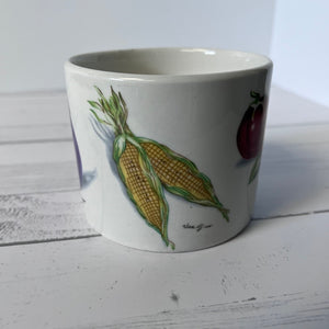 White mug with corn and tomato design on a wooden surface