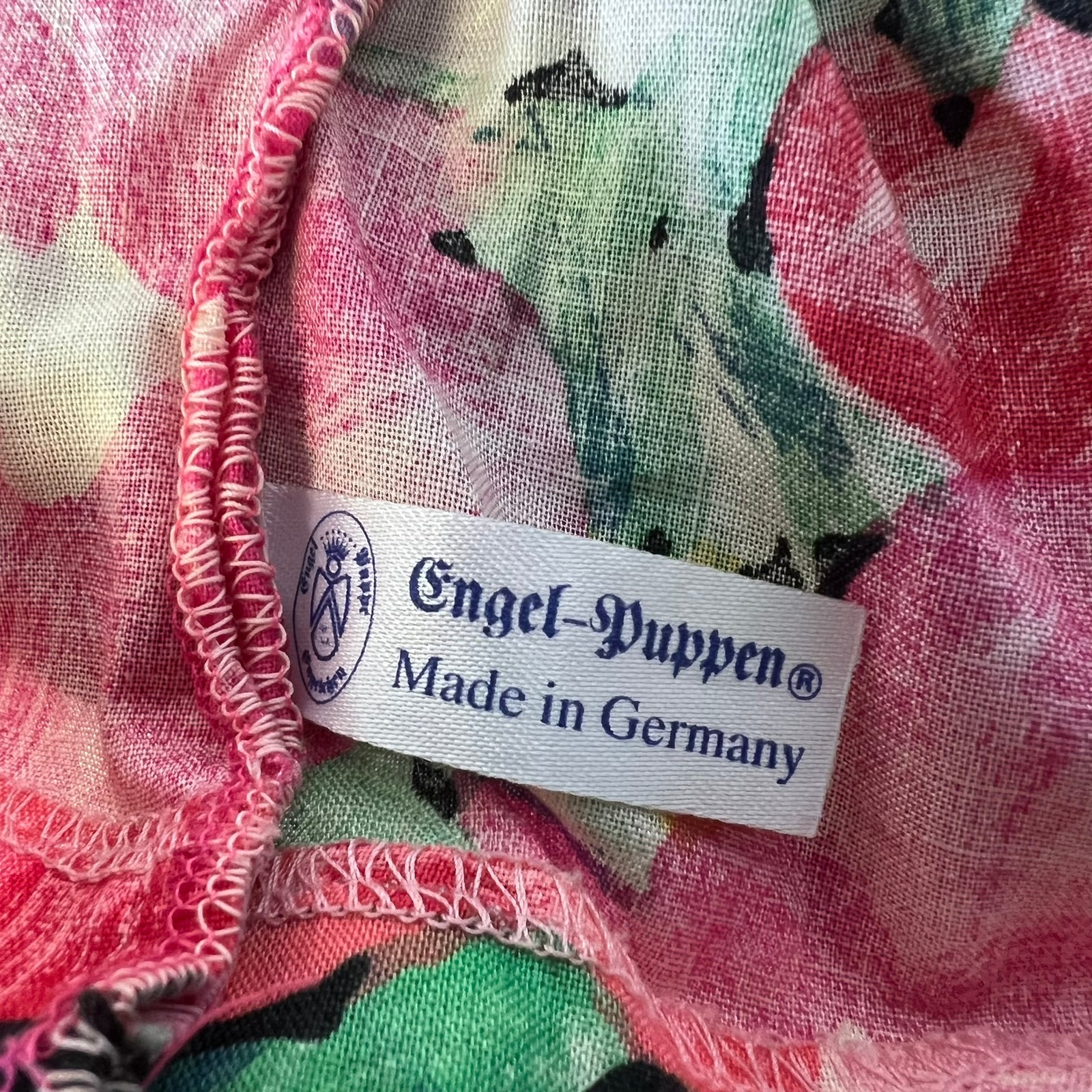 Close-up of a colorful floral fabric with a white sewn-in label reading 'Engel-Puppen Made in Germany'.