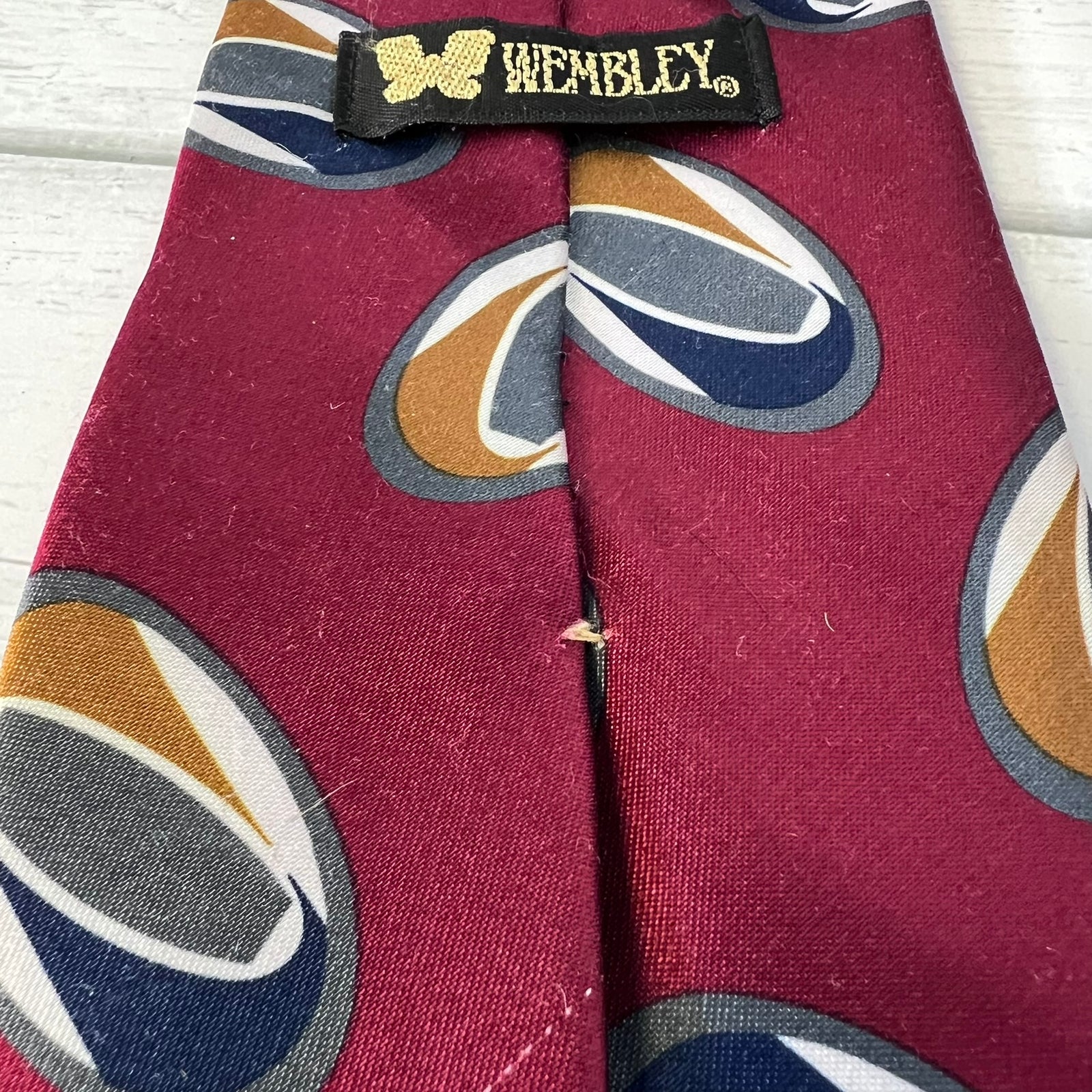 Maroon tie with multicolored circular patterns and 'Wembley' label on a wooden surface