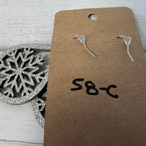 Clear earrings on a brown cardboard tag with 'S8-C' marking, snowflake ornament in the background.