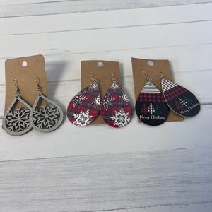 Three pairs of Christmas-themed earrings on cardboard cards against a wooden background.