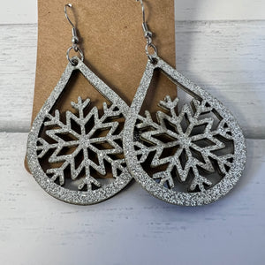 Silver snowflake earrings on a cardboard backing with a light wooden background