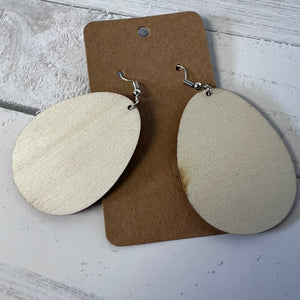 Beige earrings on a brown card against a light gray background