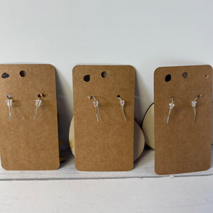 Three pairs of earrings on brown cardboard cards against a white background