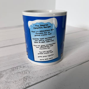 Blue mug with white interior and exterior, featuring a S'mores recipe on a light gray surface.