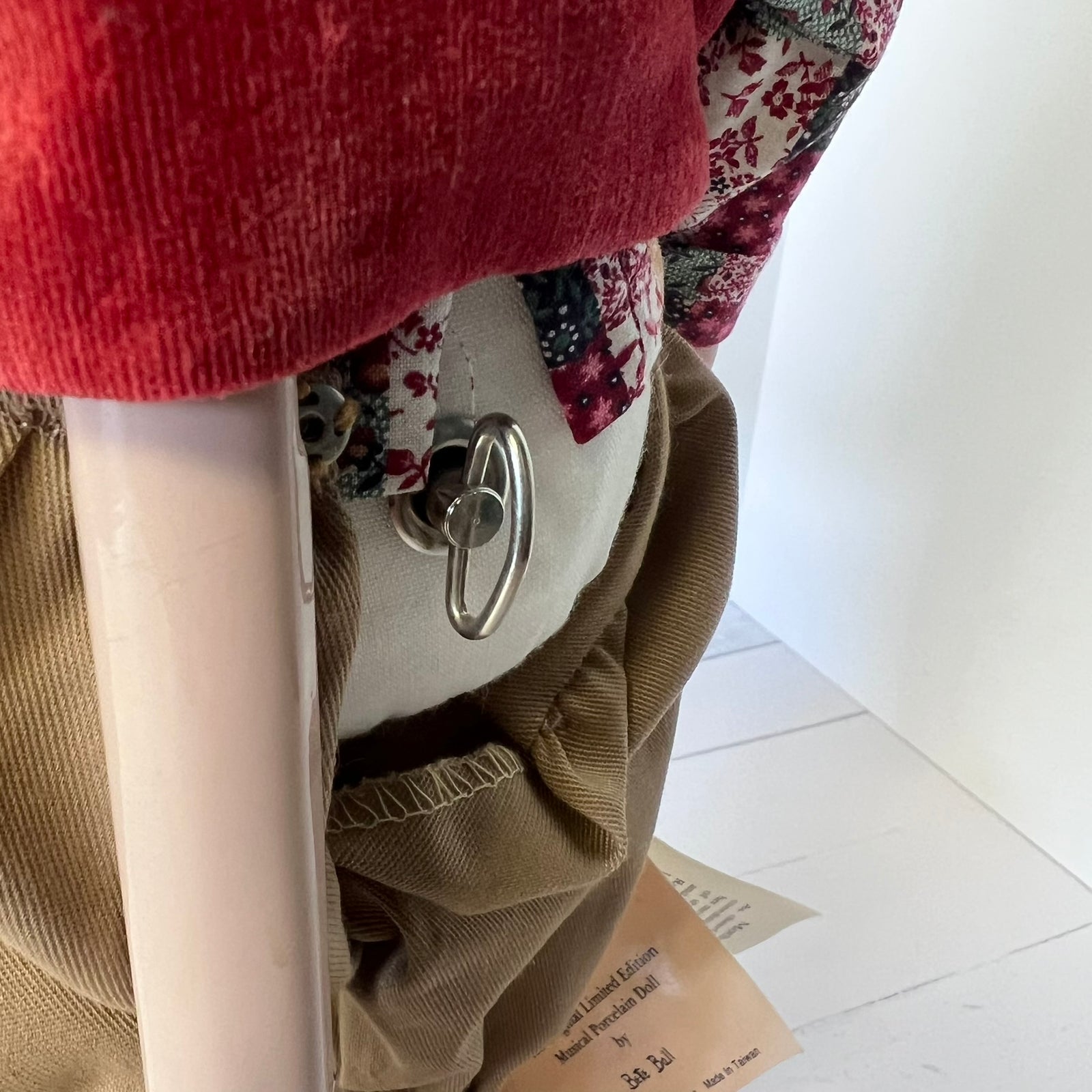 Close-up of a clothing display showing a tan corduroy garment with a floral fabric panel, a red textured fabric section, and a silver metal ring detail on a white mannequin torso.