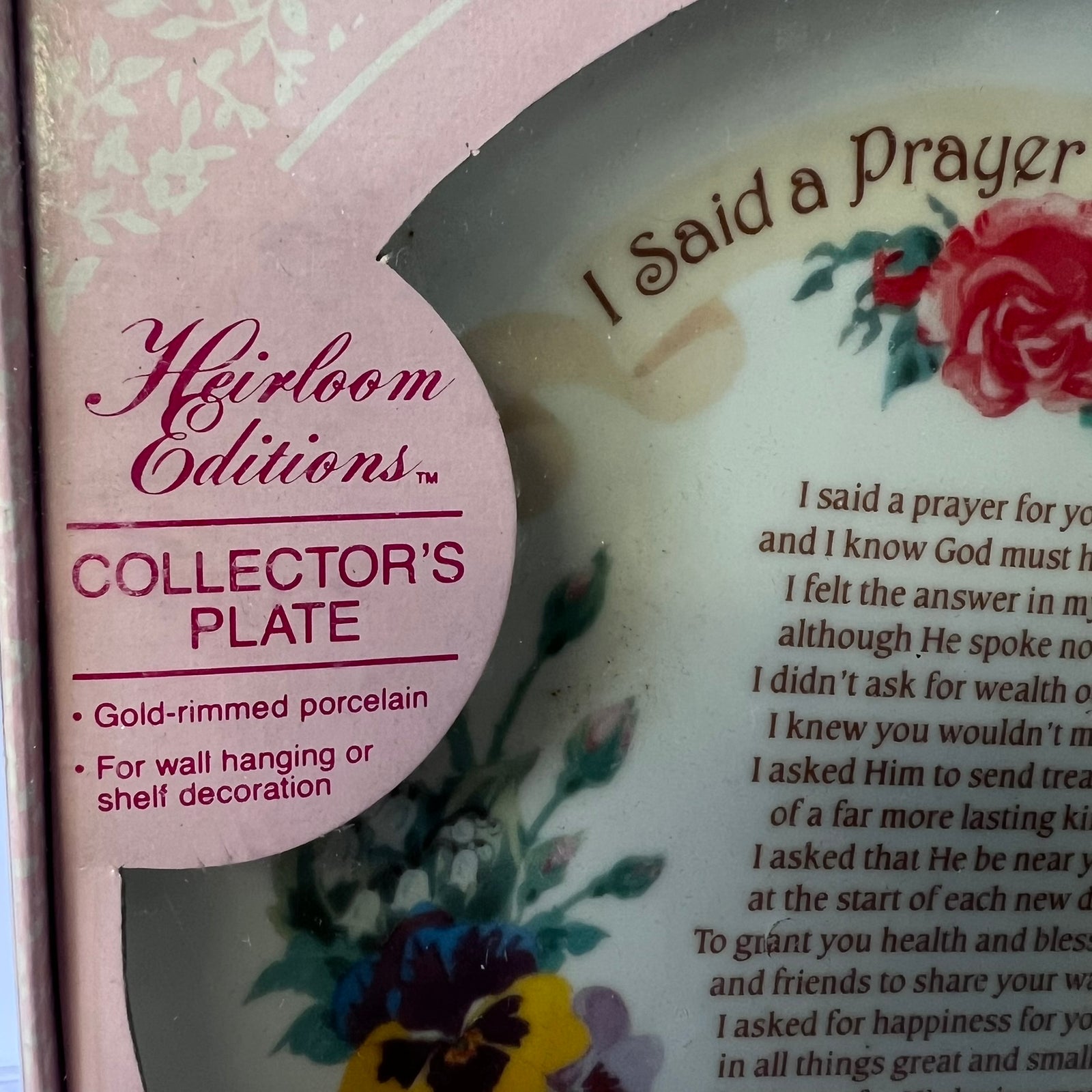 Close-up of a Heirloom Editions Collector's Plate package showing part of a gold-rimmed porcelain plate with floral artwork and printed prayer text.