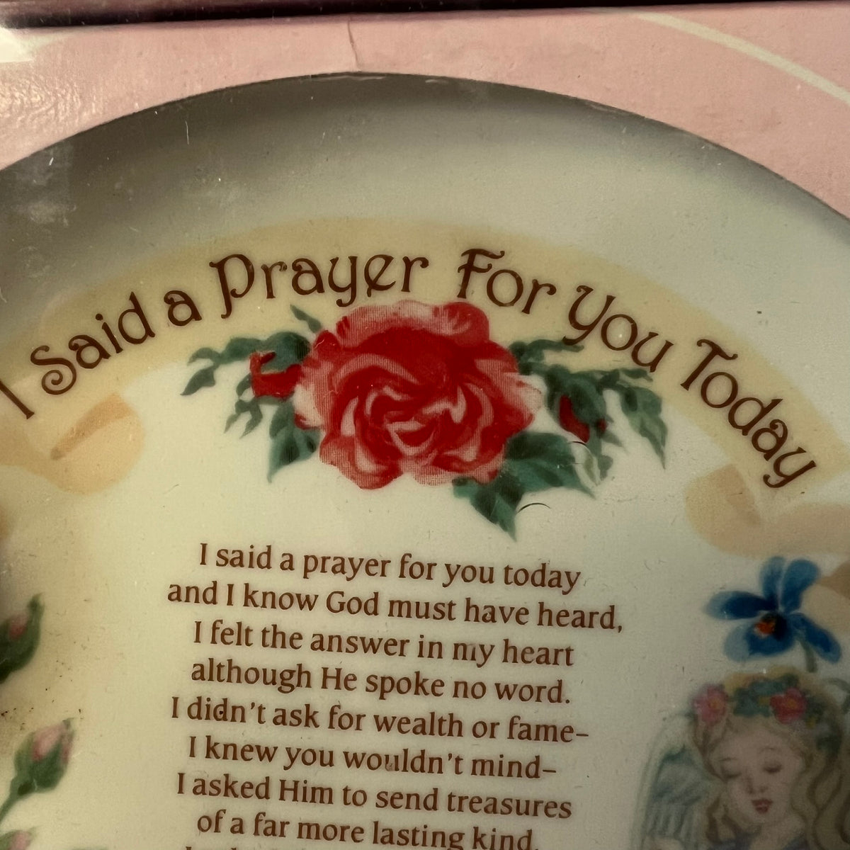 A close-up of a decorative ceramic plate with the printed phrase 'I Said a Prayer For You Today' in brown script above a red rose and a prayer text, with a small floral illustration at the lower right.