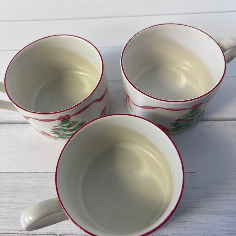 Three ceramic mugs with red rims on a white wooden surface